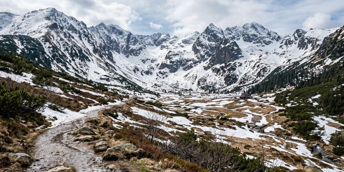Górski krajobraz w Polsce z topniejącym śniegiem na szlaku i szczytach, pokazujący moment przejścia z zimy do wiosny