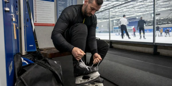 Mężczyzna sznuruje czarne łyżwy hokejowe na ławce w szatni krytego lodowiska